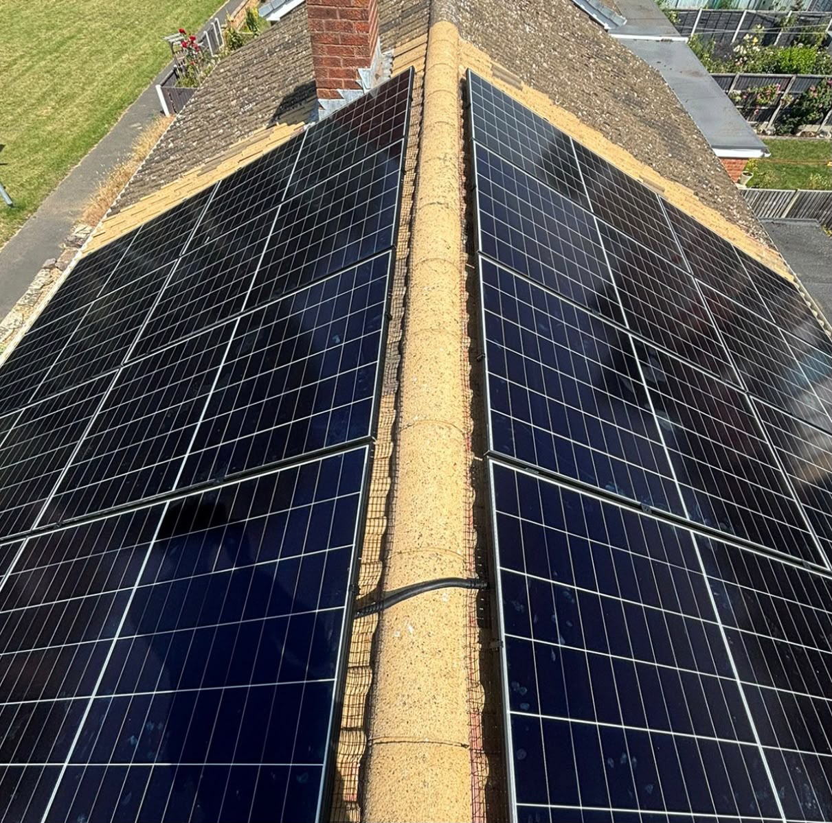 Twin black solar panel arrays installed either side of a chimney on a pitched tiled roof