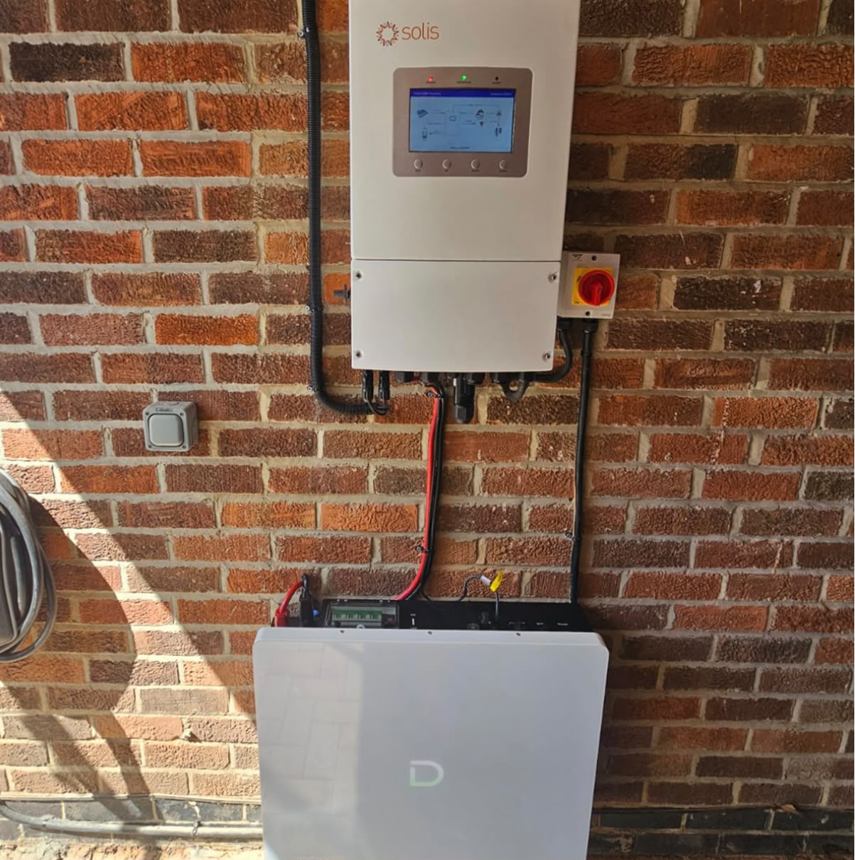 Solis inverter with a single wall-mounted lithium home battery on an exterior brick wall