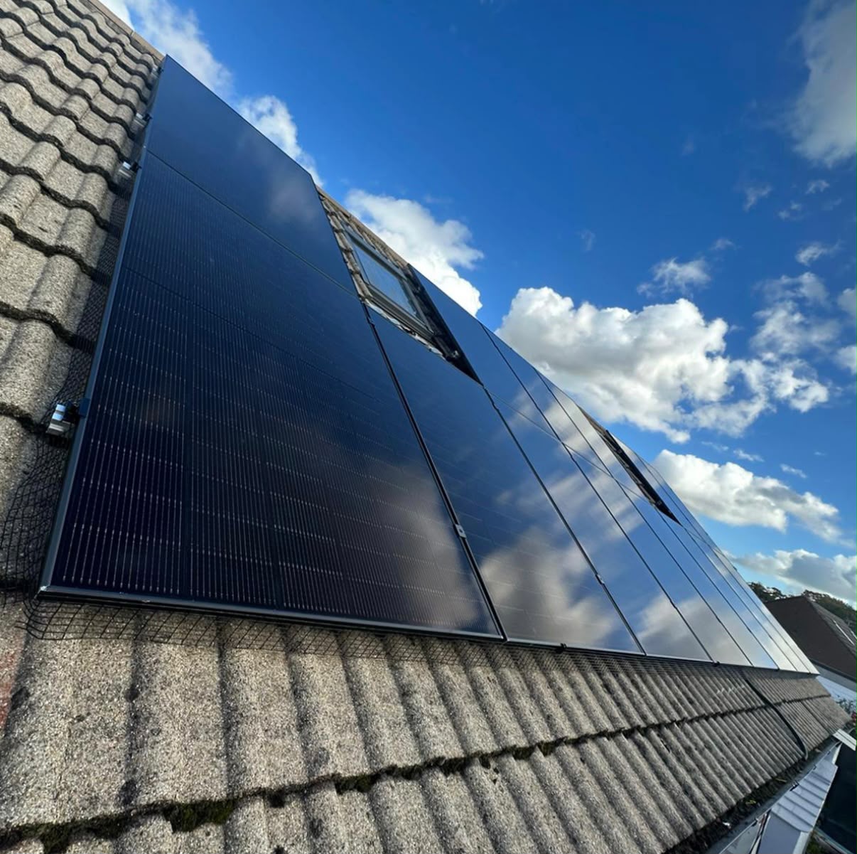 Close-up of all-black monocrystalline solar panels on a residential slate roof under blue sky