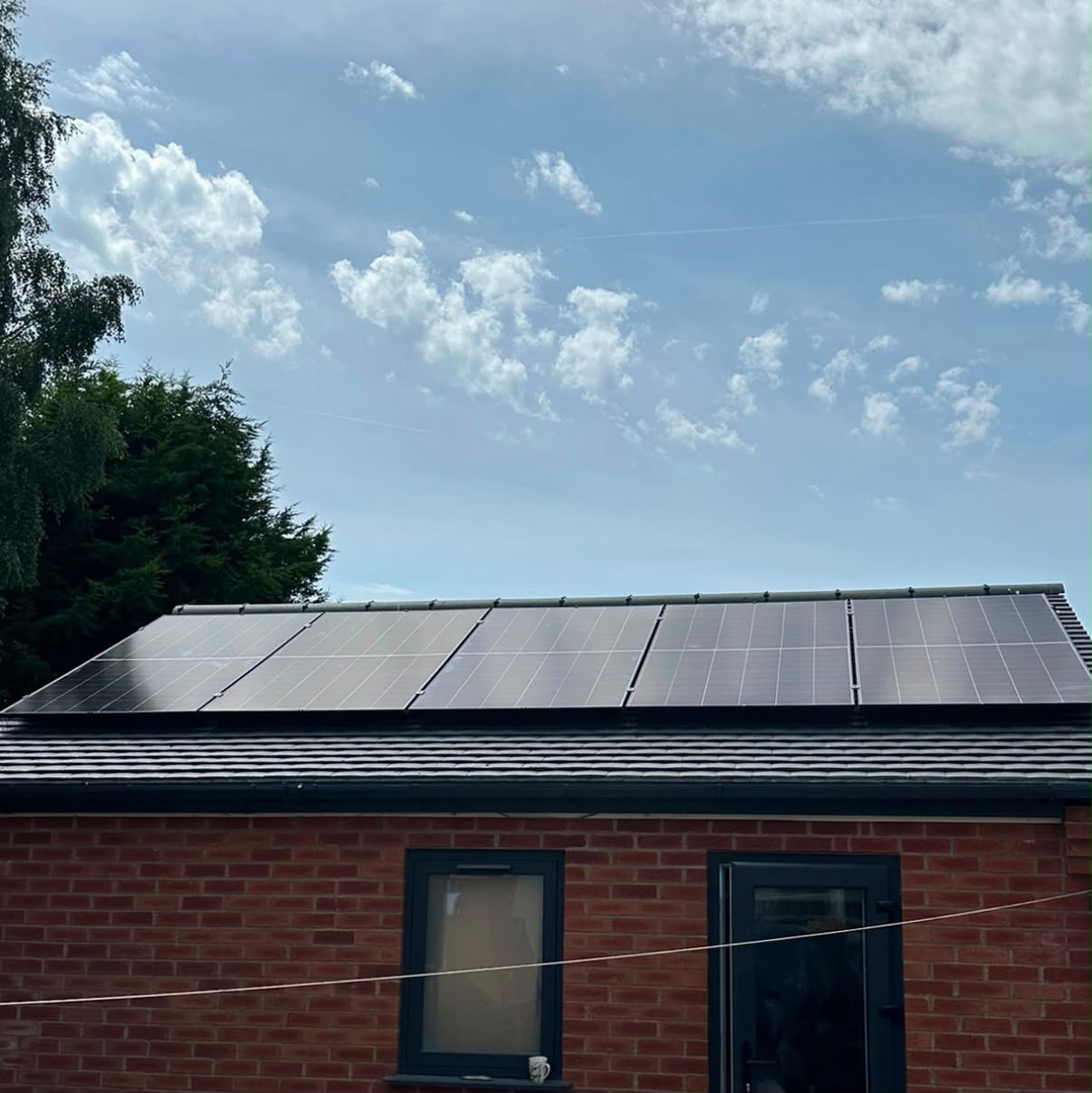 Row of solar panels along the pitched roof of a red-brick outbuilding