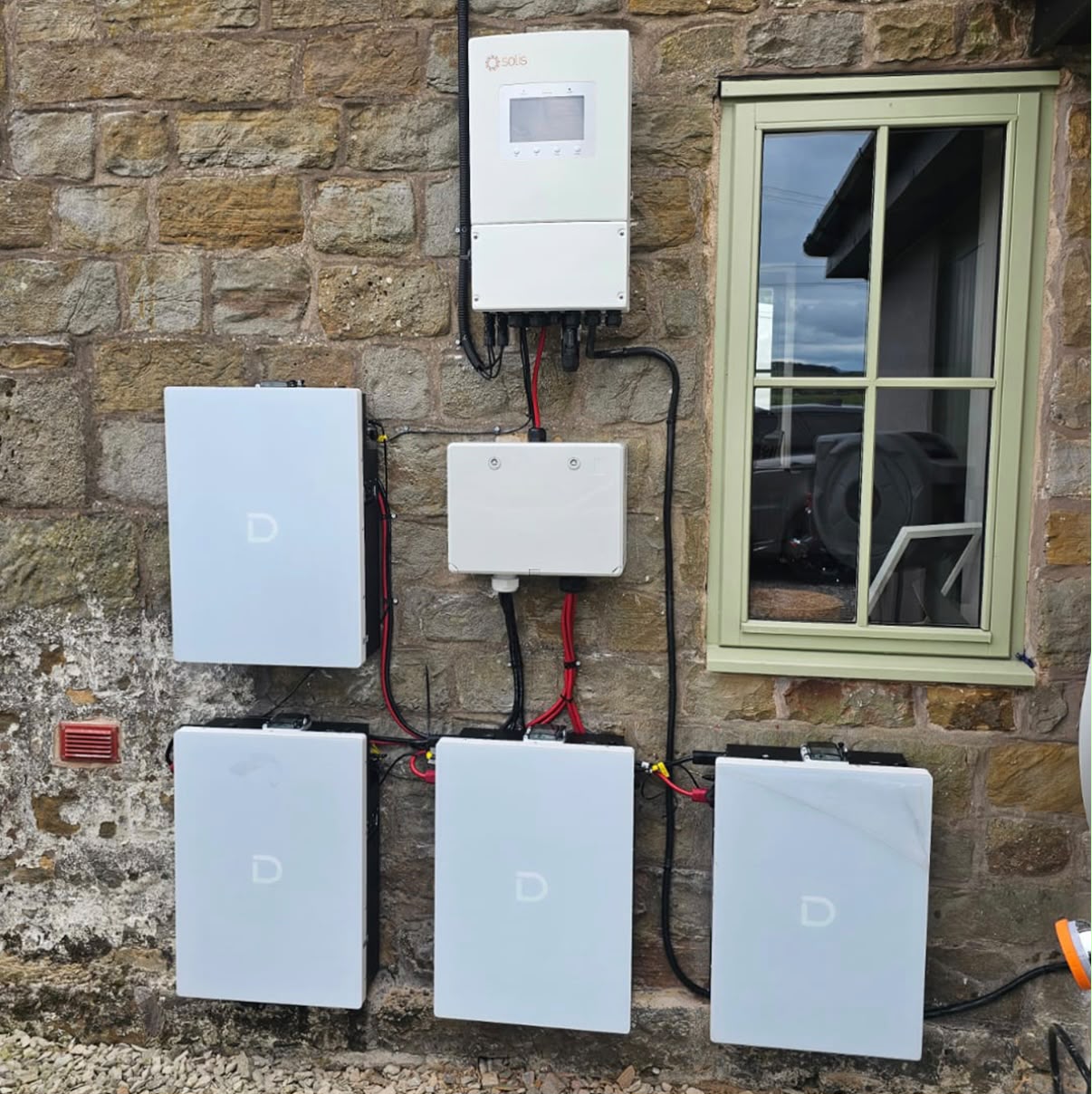Six-unit home battery storage bank with hybrid inverter on a stone cottage
