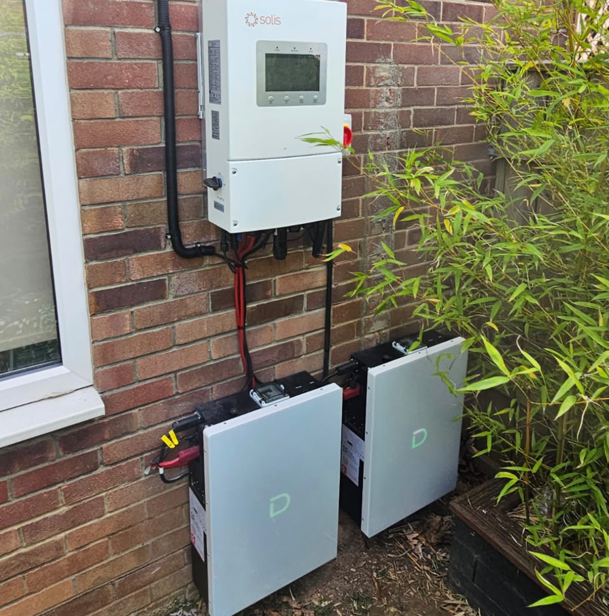Solis hybrid inverter with two home battery units installed outside a brick home